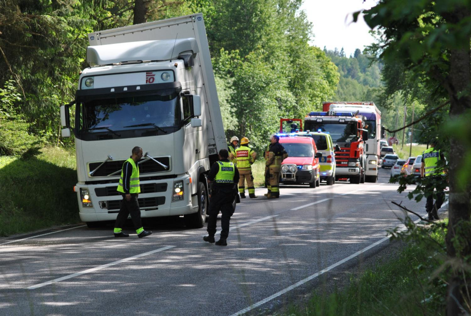 Flera utryckningsfordon och personal rycker ut till en incident med en vit lastbil på en trädkantad väg i dagsljus.
