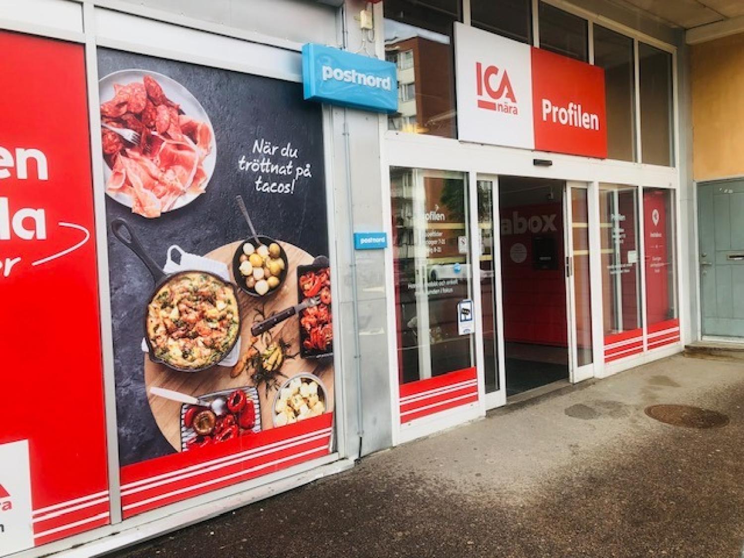 Ingången till en ICA Nära-butik med en stor livsmedelsreklam och skyltar för PostNords posttjänster vid dörren.