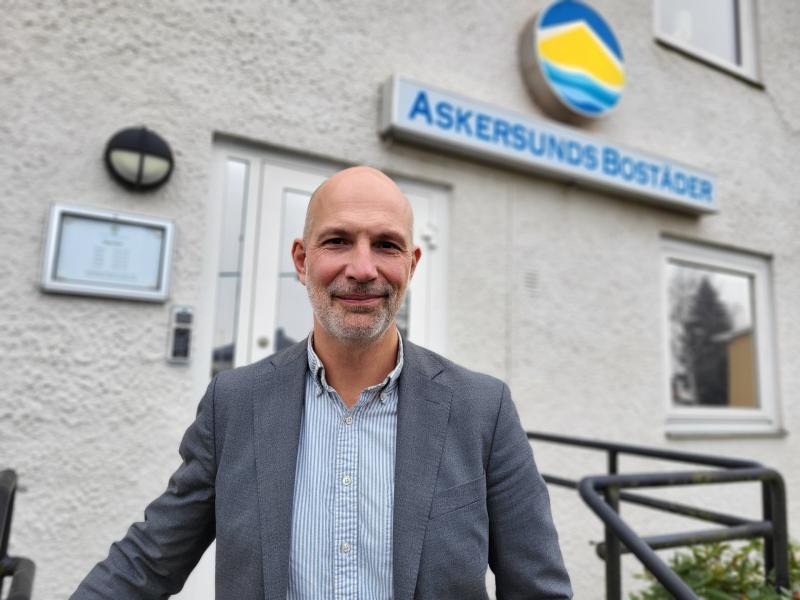 En man i kostym står framför en byggnad med en skylt där det står 