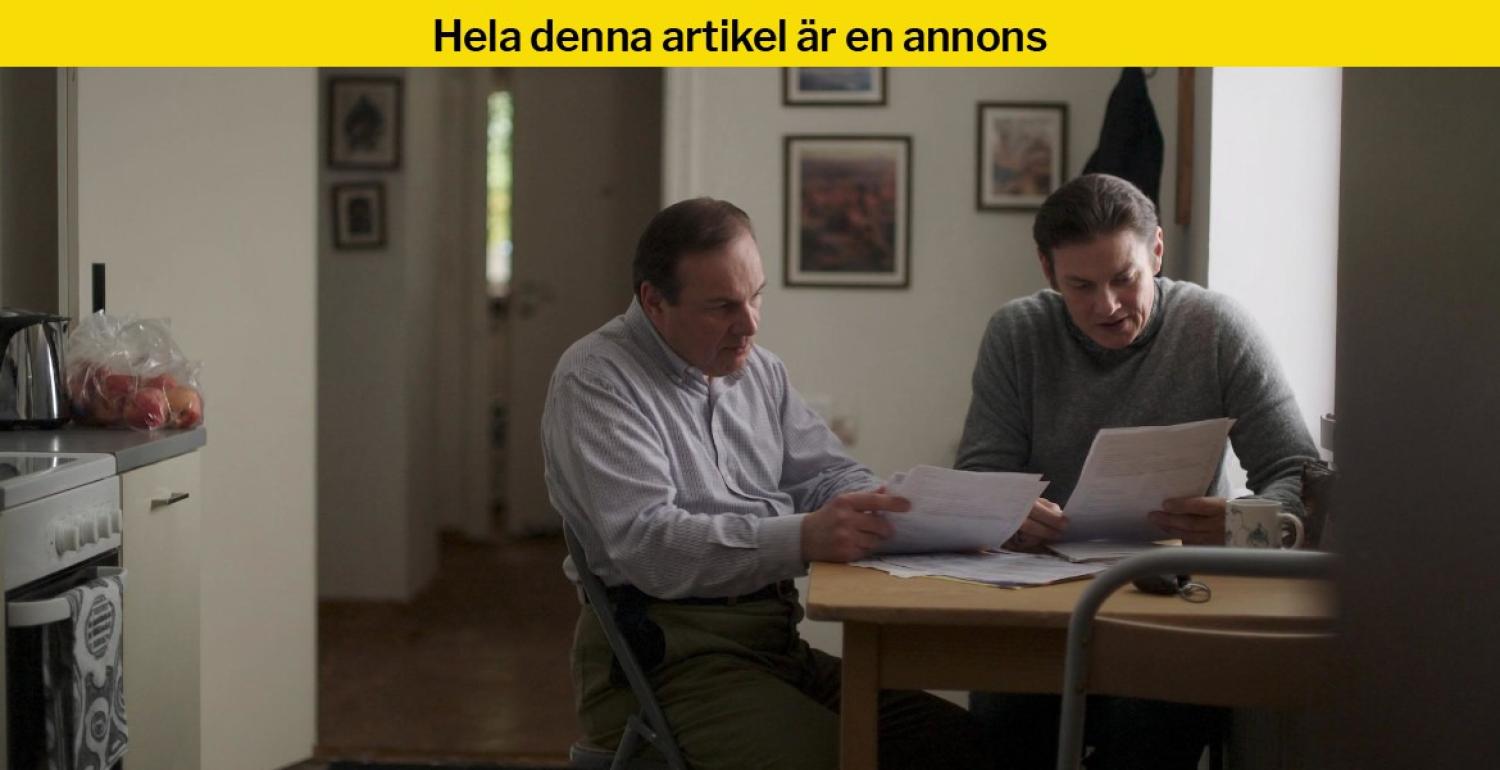 Två män sitter vid ett köksbord och går igenom papper tillsammans; en skål med äpplen och fler dokument syns i närheten.