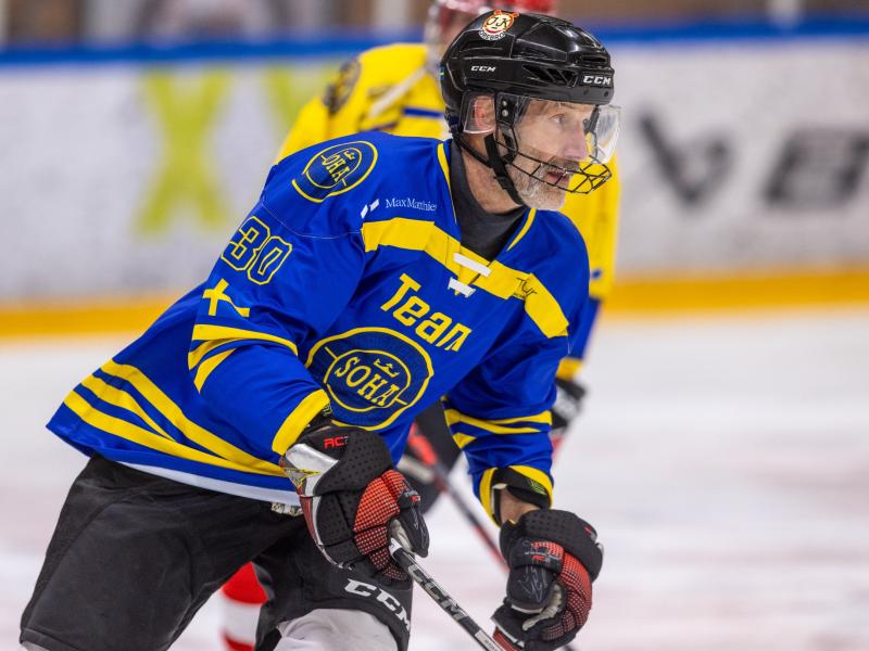 En manlig ishockeyspelare i blågul tröja, med hjälm och handskar, åker skridskor på isen under en match.