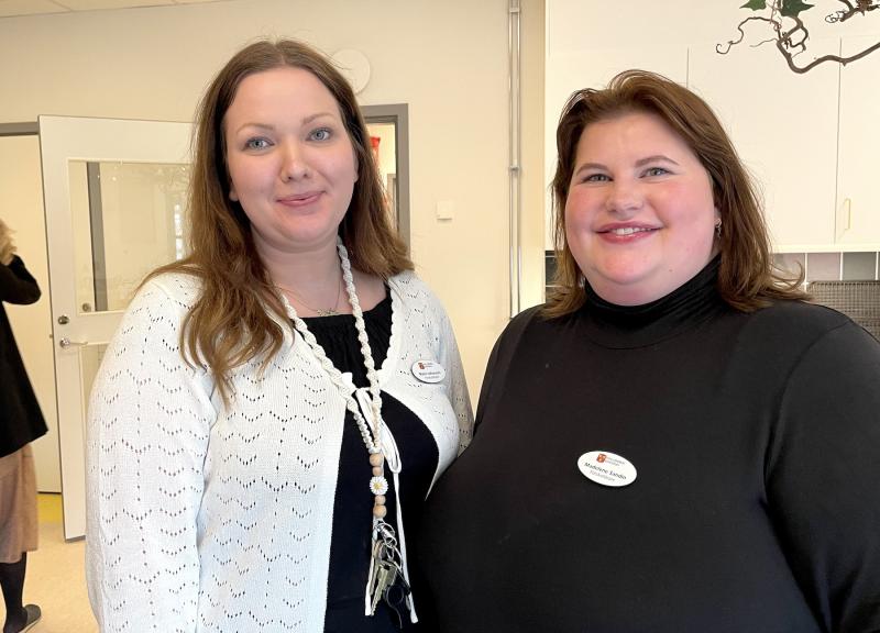 Två kvinnor som ler mot kameran, den ena i en vit kofta och den andra i en svart polotröja, båda med namnbrickor.
