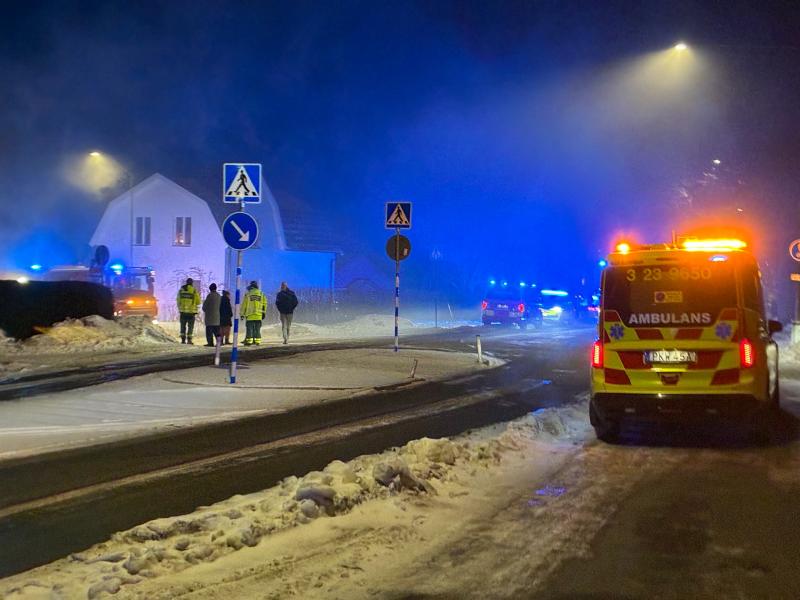 Utryckningsfordon med blinkande ljus och personal är närvarande på en snöig gata nära ett hus på natten.