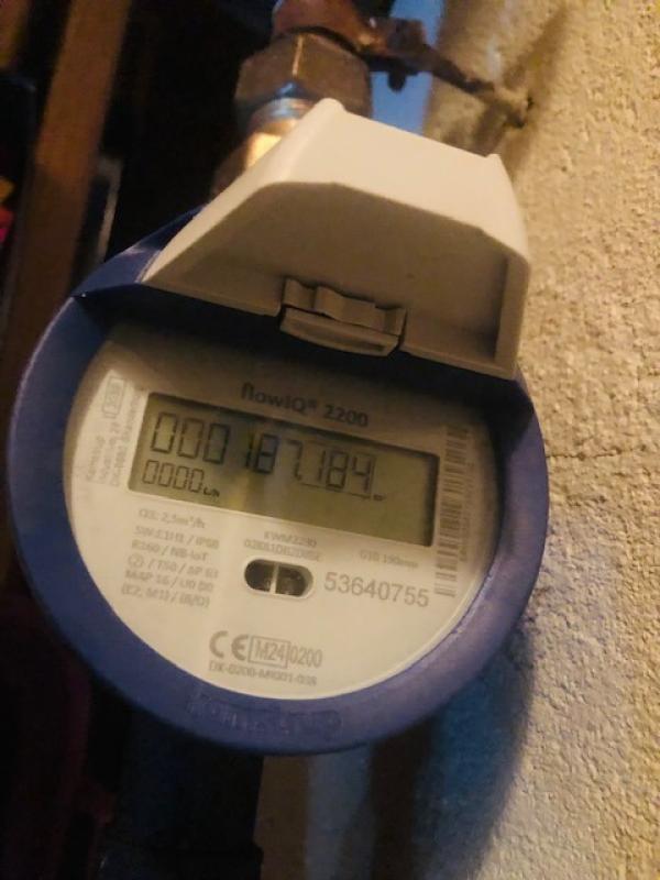 En närbild av en digital vattenmätare som visar 187184. Enheten är monterad på en vägg med ett rör fäst ovanför den.