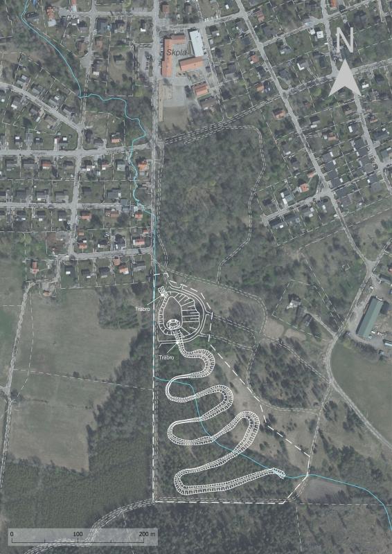 Flygfoto över en stad med en park med slingrande stigar. Bostadsområden ligger till vänster och ett stort öppet grönområde med träd till höger. En nordpil finns uppe till höger.
