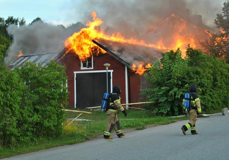 Två brandmän som står framför ett brinnande hus.