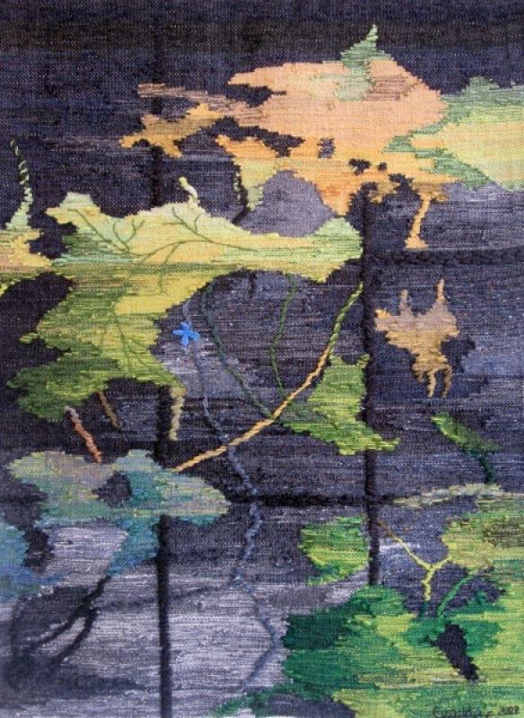 Ett konstverk i vävd textil föreställer gröna och gula blad med stjälkar och skuggor mot en mörk, strukturerad bakgrund.