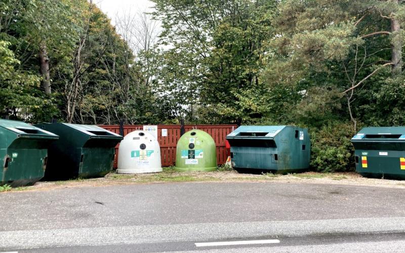 En rad med gröna återvinningskärl på en parkeringsplats.