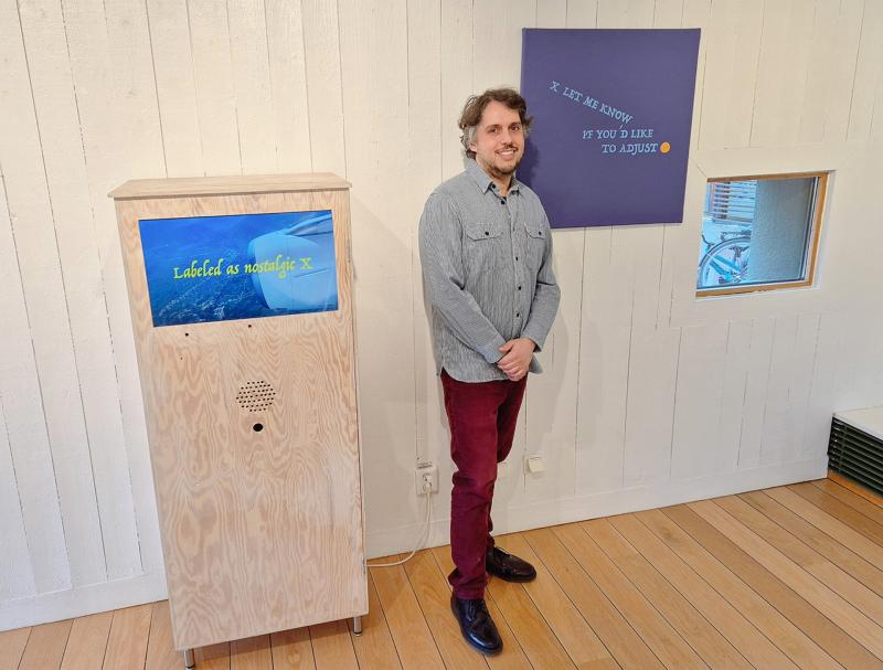 En man står inomhus bredvid en trälåda med en skärm där det står 