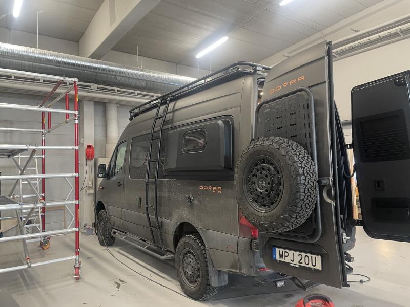 En dammig, svart terrängbil med reservdäck monterat på baksidan står parkerad inne i ett garage.