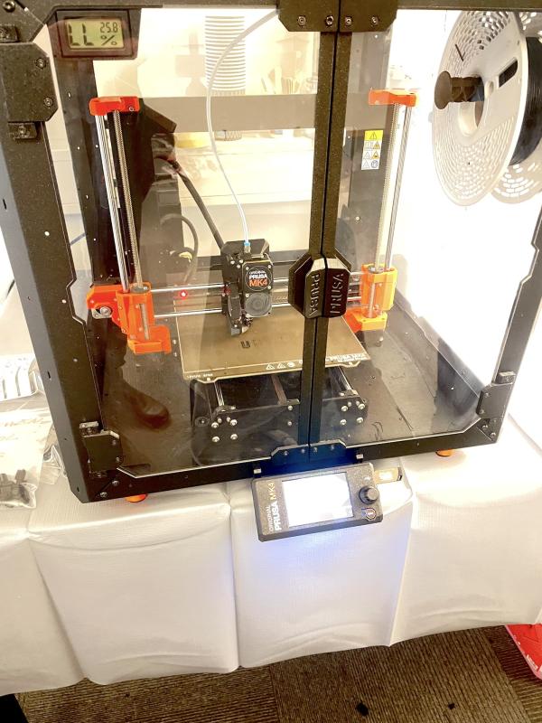 En 3d-skrivare med en svart filamentrulle, mid-print inne i ett slutet utskriftsområde.