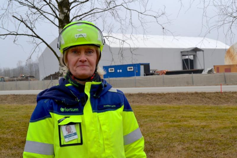 Kvinnlig byggnadsarbetare med skyddshjälm och reflekterande jacka som står på en arbetsplats.