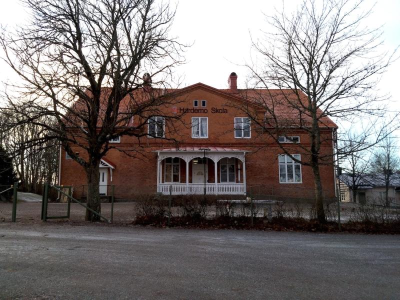 En byggnad i rött tegel med en veranda i trä och en skylt där det står 