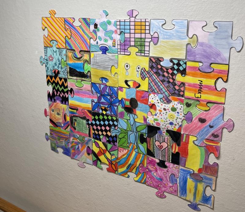 Ett färgglatt, handritat pussel är monterat på en vit texturerad vägg, där varje bit uppvisar unika abstrakta mönster och designer.