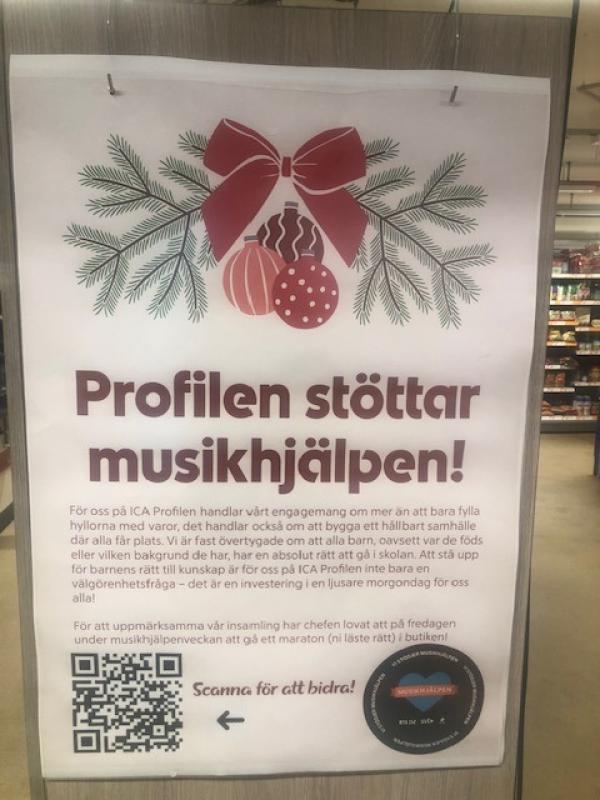 Affisch i butik med julmotiv som berättar att Profilen stödjer Musikhjälpen och uppmanar till att skanna en QR-kod för att skänka pengar, med text på svenska.