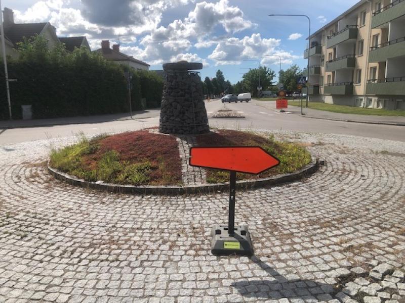 En rondell med ett stenmonument i mitten, där en stor orange pil pekar åt höger på kullerstensytan.