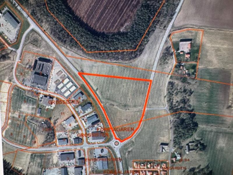 Flygbild över en triangulär tomt som är markerad med rött, omgiven av vägar, byggnader, åkrar och bostadsområden.