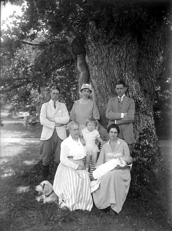 Ett svartvitt foto av en familj som poserar framför ett träd.