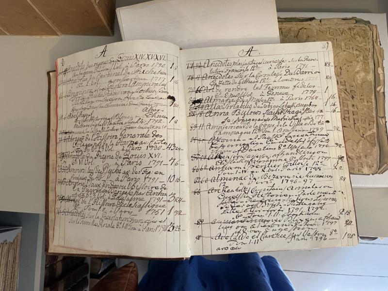 En öppen huvudbok med handskrivna anteckningar i kursiv skrift på båda sidorna, med namn och datum. Boken ligger på ett bord med andra dokument i närheten.