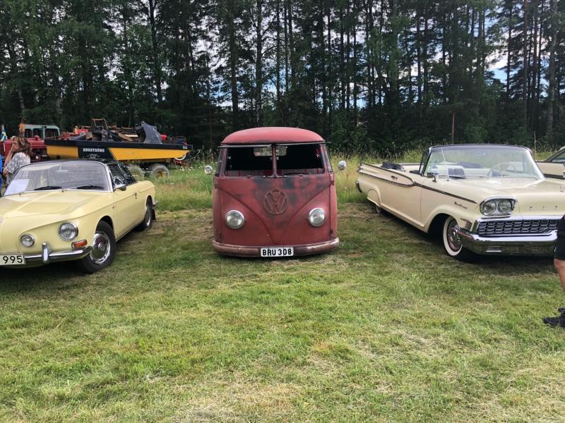Tre veteranbilar – en gul coupé, en röd Volkswagen-skåpbil och en krämfärgad cabriolet – stod parkerade på gräsmattan med träd och gamla maskiner i bakgrunden.