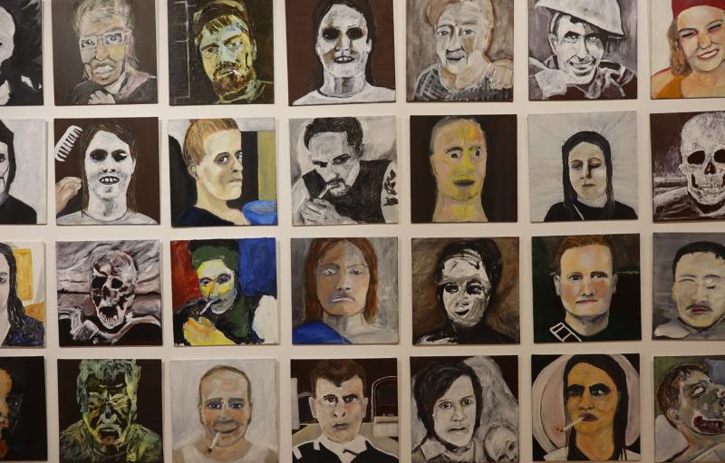 Ett rutnät av målade porträtt, vart och ett föreställande en annan person med olika ansiktsuttryck och konstnärliga stilar, vissa realistiska och andra abstrakta eller skelettliknande.