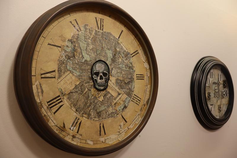 Två väggklockor; den vänstra klockan har romerska siffror och en dödskalle i mitten, medan den högra klockan har standardsiffror och ett slitet utseende.
