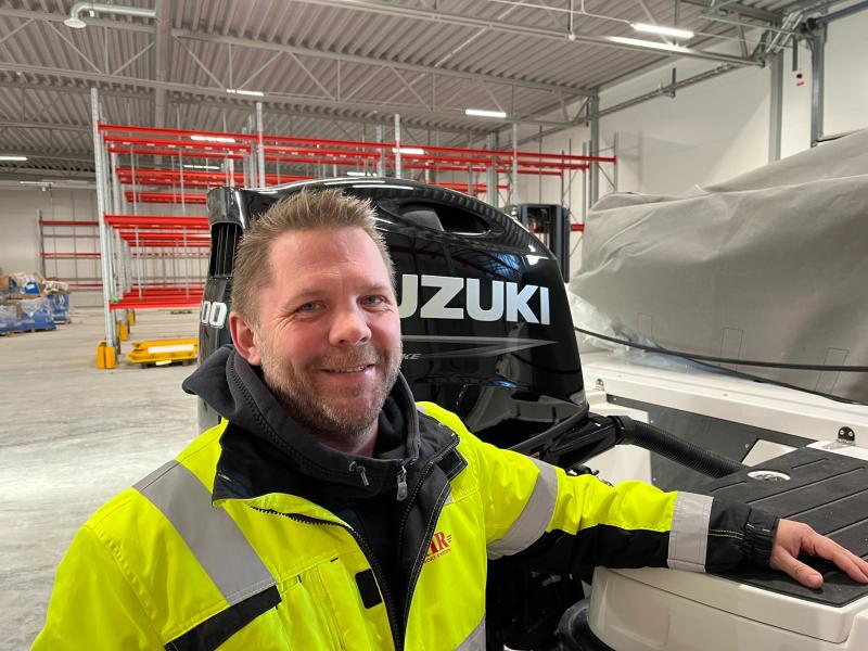 En man i varseljacka står inomhus bredvid en båtmotor märkt 