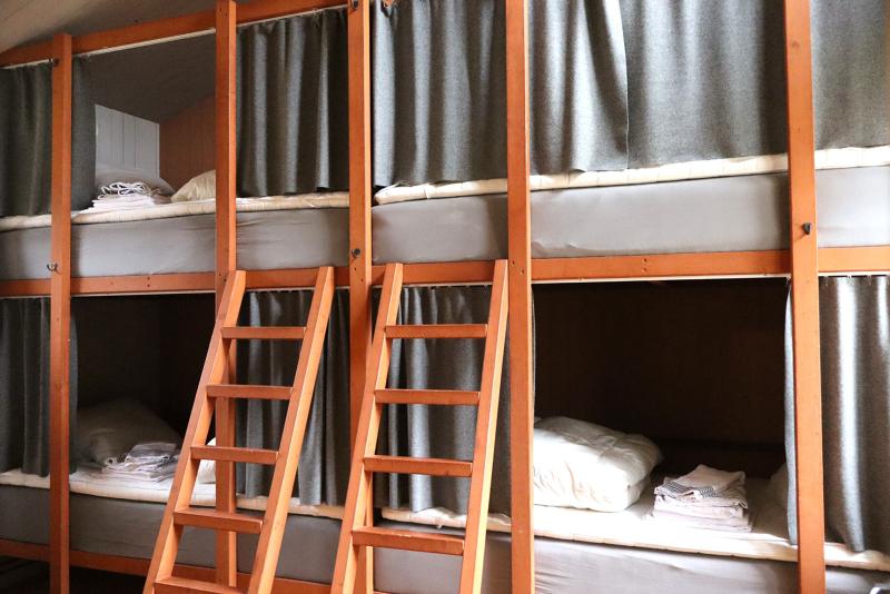 Två uppsättningar våningssängar i trä med grå gardiner, stegar och prydligt arrangerade sängkläder i ett delat rum.