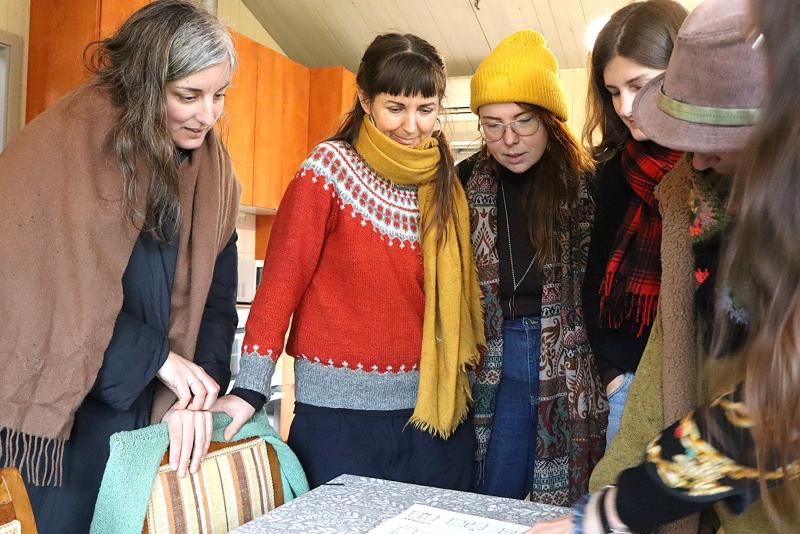 Fem kvinnor står tätt runt ett bord och tittar på papper eller dokument som ligger framme i ett varmt upplyst rum.