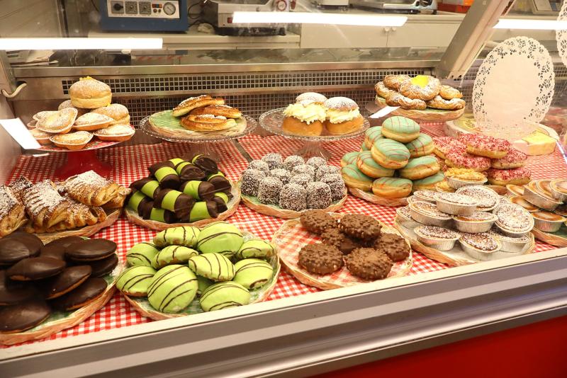 En bagerivitrine med olika bakverk, munkar, kakor, småkakor och sötsaker upplagda på tallrikar över en rödrutig duk.