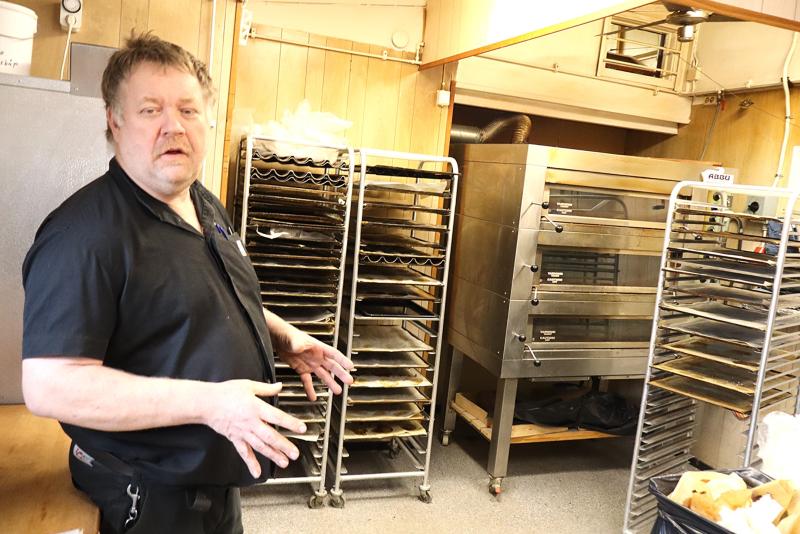 En man står i ett storkök bredvid tomma bakgaller och en stor ugn i rostfritt stål.