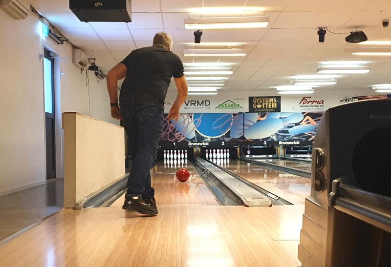 En man kastar ett rött klot på en bowlingbana i en bowlinghall inomhus och siktar på en uppsättning käglor.