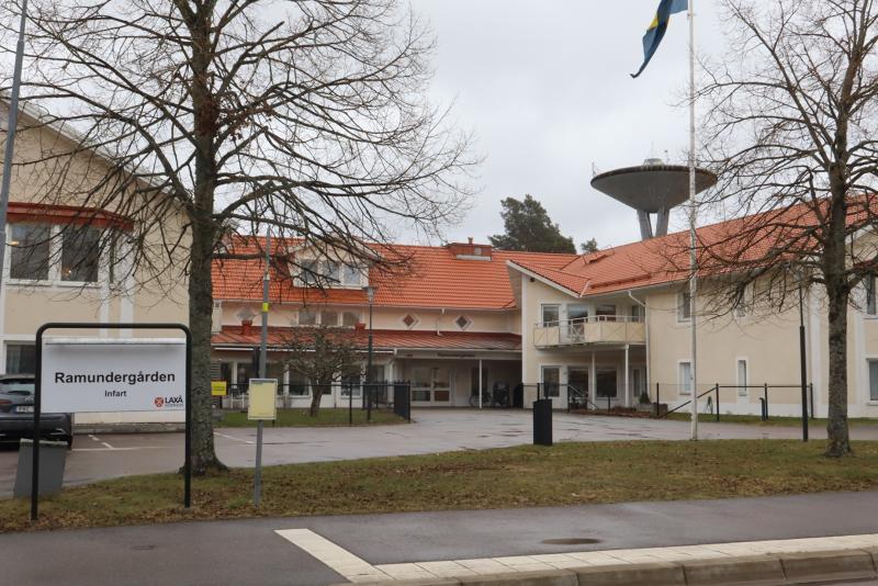 En beige tvåvåningsbyggnad med rött tak, en flaggstång, ett vattentorn i bakgrunden och en skylt med texten 