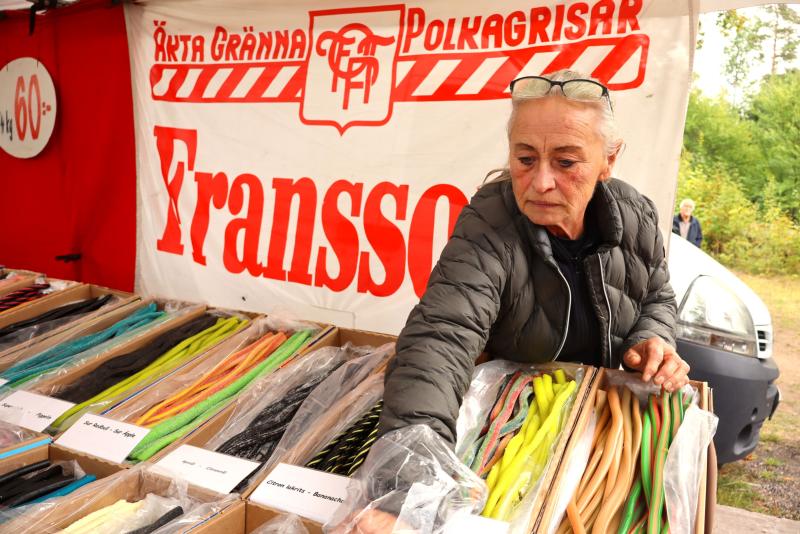 En kvinna väljer lakritsgodis från ett stånd med olika sötsaker på en marknad, med en skylt med texten 
