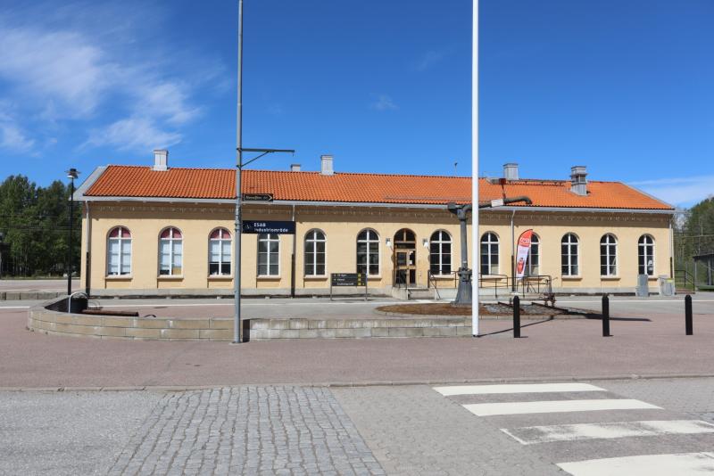 En tågstationsbyggnad i gult tegel med rött tegeltak, välvda fönster och en skylt med texten 