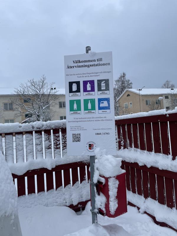 En snötäckt skylt framför ett staket.