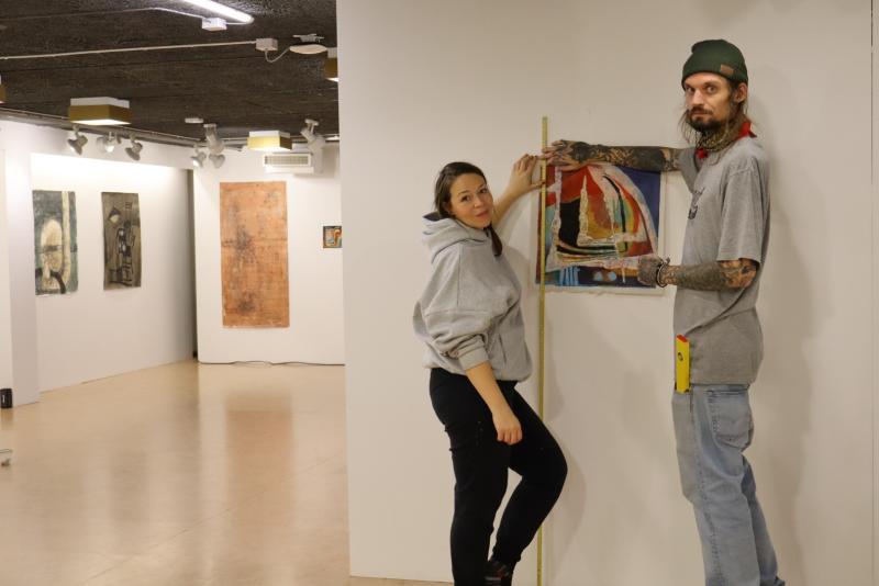 Två personer hänger konstverk i ett galleri med hjälp av ett måttband för justering.