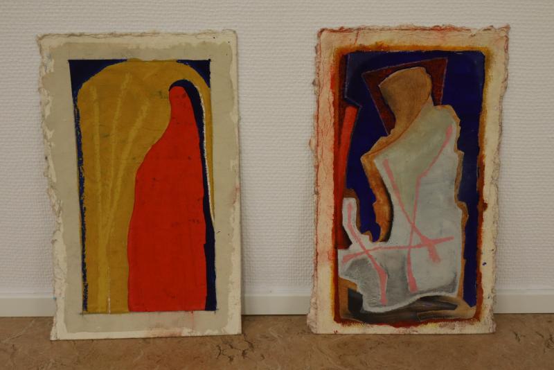 Två abstrakta målningar lutade mot en vit vägg, med djärva former och färger med strukturerade ytor.