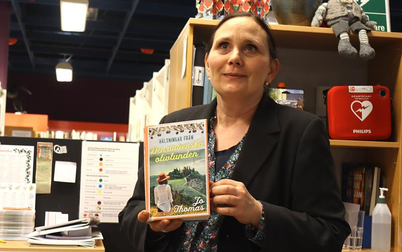 En person i svart kavaj håller upp en bok med titeln 
