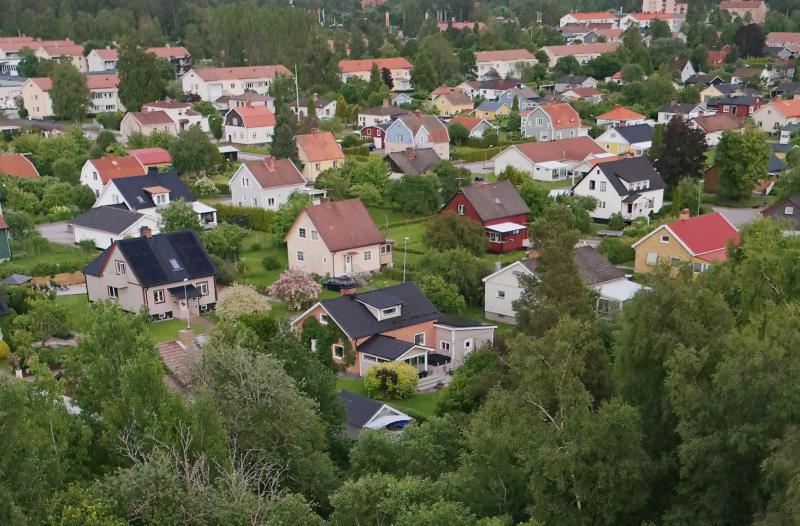 Flygbild över ett förortsområde med hus omgivna av träd och grönska.