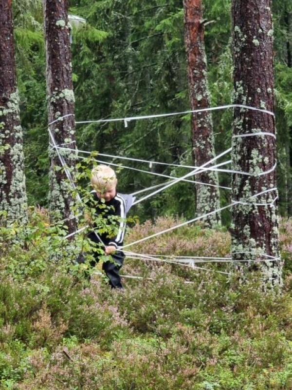 En person trasslade in i vit tejp mellan träd i ett skogsområde.