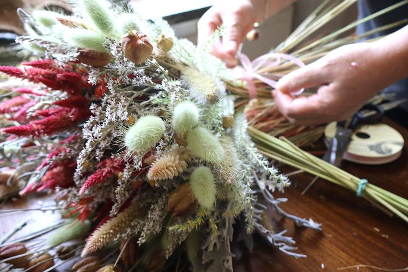 En person ordnar en bukett med torkade blommor på ett träbord, med en sax och ett band bredvid sig.