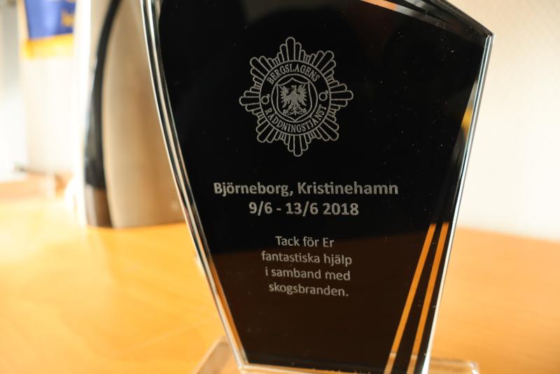 En svart och klar pokal med graverad svensk text som tackar för hjälpen vid skogsbranden i Björneborg, Kristinehamn, daterad 9/6 - 13/6 2018.