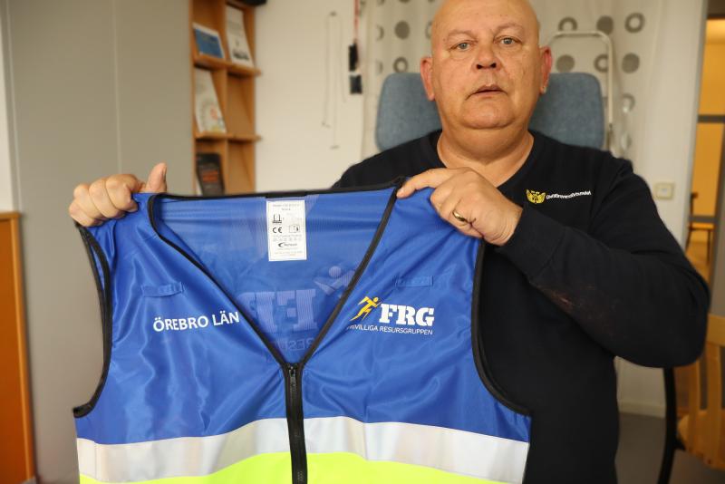 En man håller upp en blågul säkerhetsväst märkt 