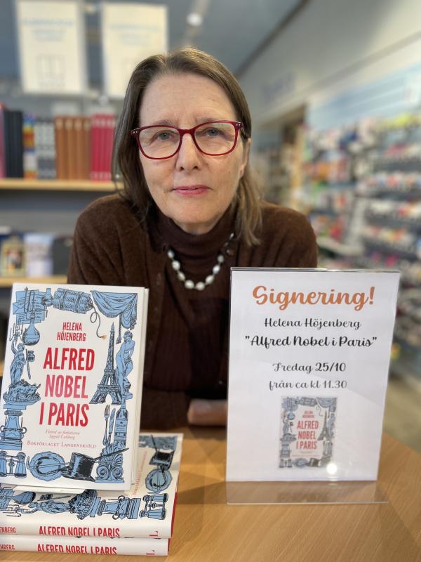 En kvinna sitter vid ett bord med en hög böcker med titeln 