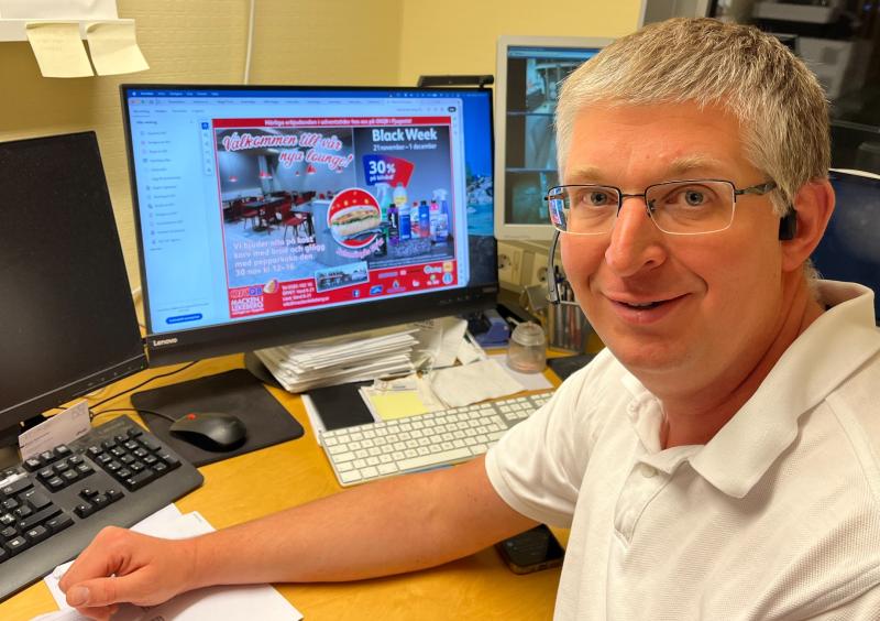 En man med glasögon sitter vid ett skrivbord framför en datorskärm som visar en kampanjannons och Black Week-rea.