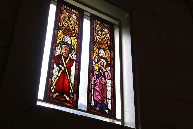 Glasmålning föreställande två religiösa figurer som håller i föremål, inramat av en fönsteröppning av sten, med ljusinsläpp.