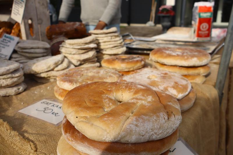 Flera runda flatbröd ligger uppställda på ett bord på en utomhusmarknad, och i bakgrunden syns ytterligare flatbröd samt en påse mjöl.