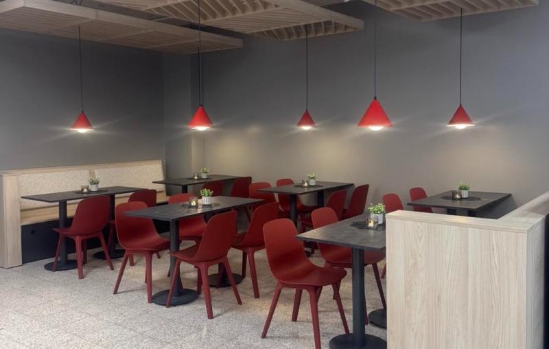 En modern caféinredning med röda stolar och pendellampor, svarta bord, ljusa trädetaljer och små krukväxter på varje bord.