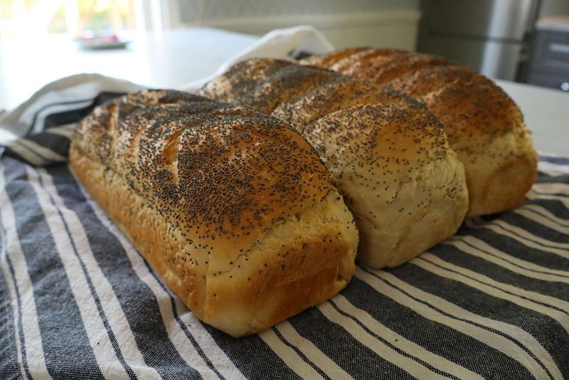 Två bröd med vallmofrön på toppen vilar på en randig duk på en köksbänk.